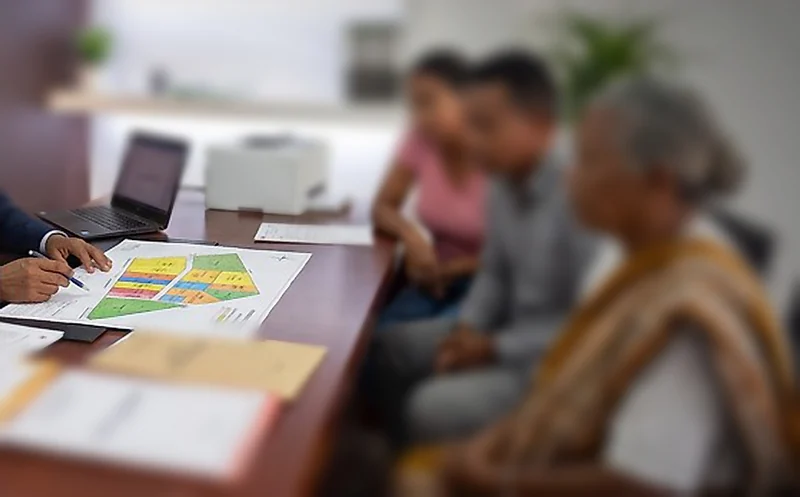 La main de l’expert annote le plan de partage d’un terrain, devant la famille